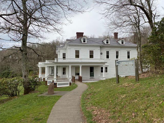 a historic white mansion sits on a green hill