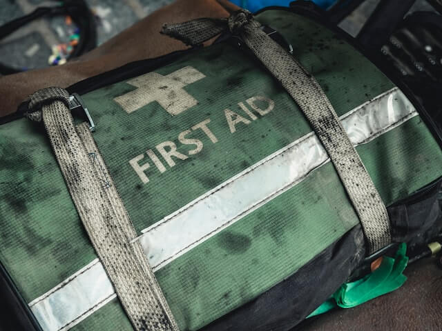 A dirty and well-worn green and white bag with first aid printed on it
