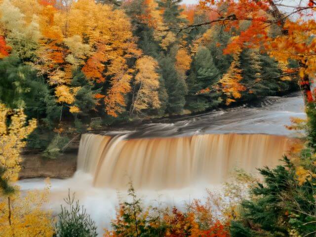 brown waterfall edged by autumn leaves