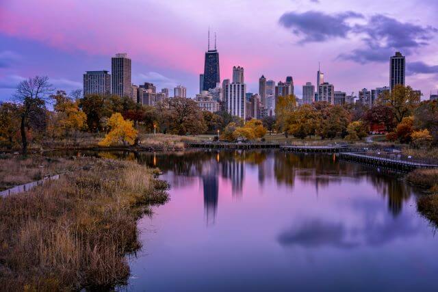 a city skyline at sunset reflected in a pond