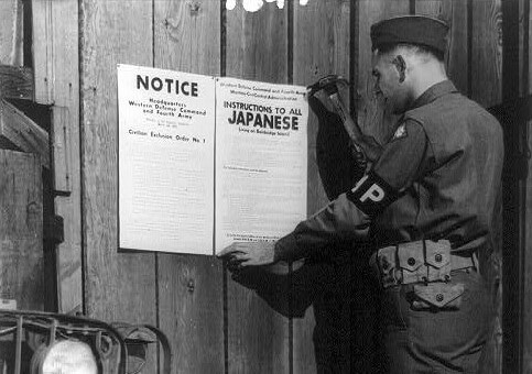 a soldier posts a sign ordering japanese americans to leave their homes