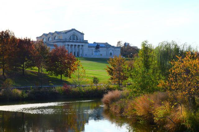 a large historic building beside a lake lined with trees