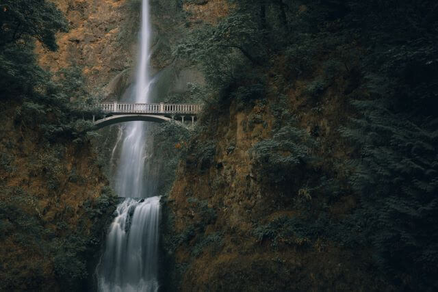 tall thin waterfall behind a bridge