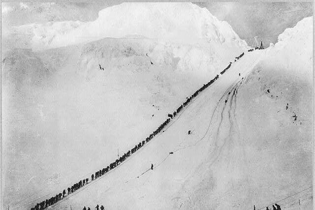 a line of tiny hikers summitting a large mountain